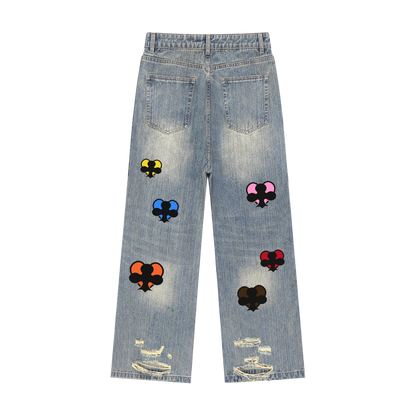 Light wash blue denim jeans shown from the back, featuring distressed rips at the hem, classic back pockets, and multiple colorful embroidered playing card patches on the legs.