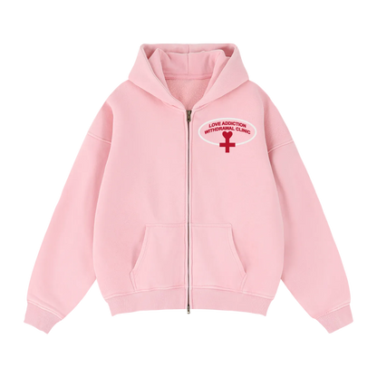 A light pink zip-up hoodie with a red and white graphic on the left chest reading 'LOVE ADDICTION WITHDRAWAL CLINIC' with a red cross symbol.