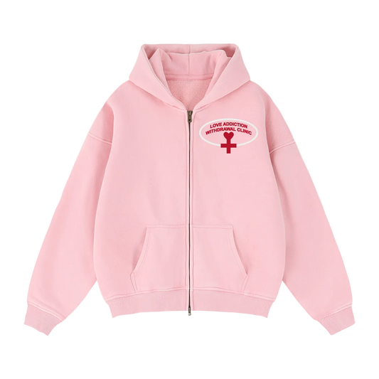 A light pink zip-up hoodie with a red and white graphic on the left chest reading 'LOVE ADDICTION WITHDRAWAL CLINIC' with a red cross symbol.