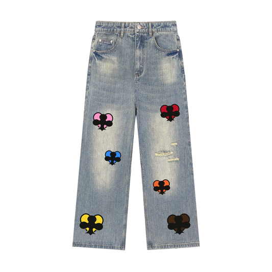 Light blue denim jeans with distressed rips and colorful embroidered patch designs featuring black spades with pink, red, blue, orange, yellow, and dark brown details, shown flat on a white background.